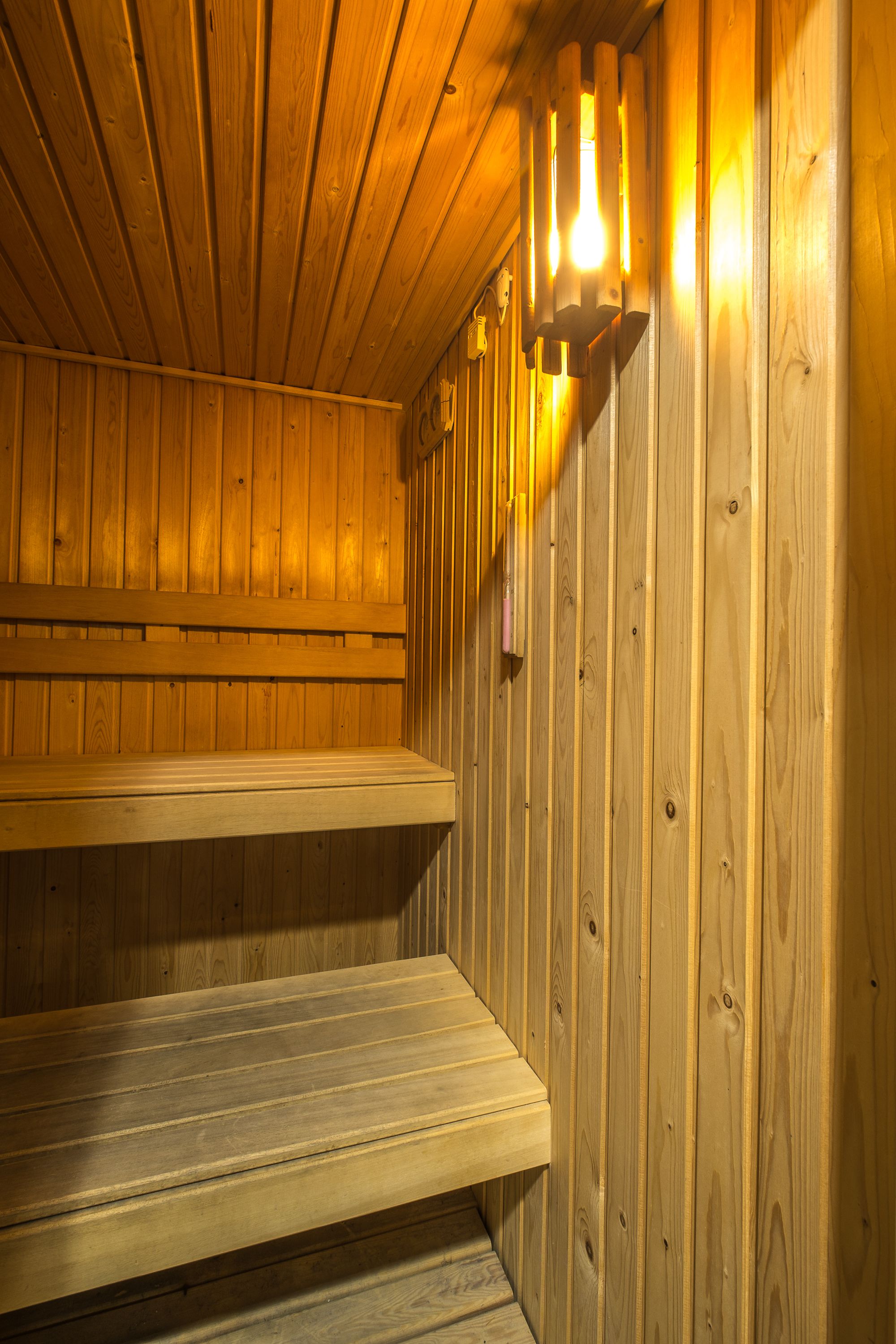 A wooden sauna with benches and a wall-mounted light fixture.