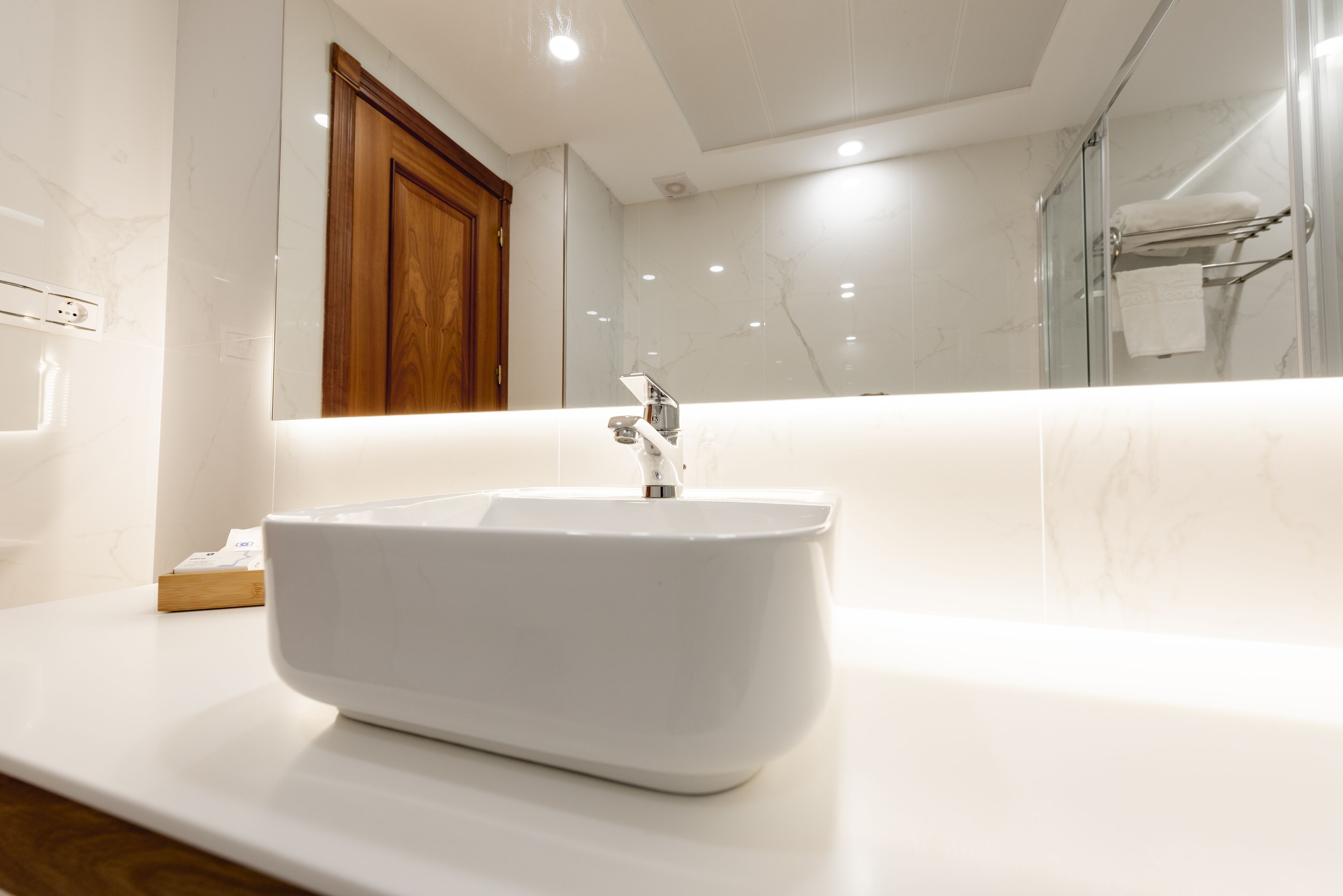 Een moderne badkamer met een witte wastafel, een houten kast en een glazen douchecabine.