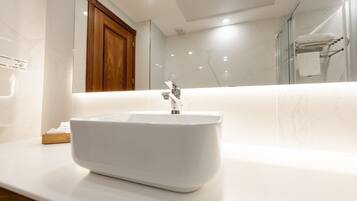 Un baño moderno con un lavamanos blanco, un mueble de madera y una cabina de ducha de vidrio.