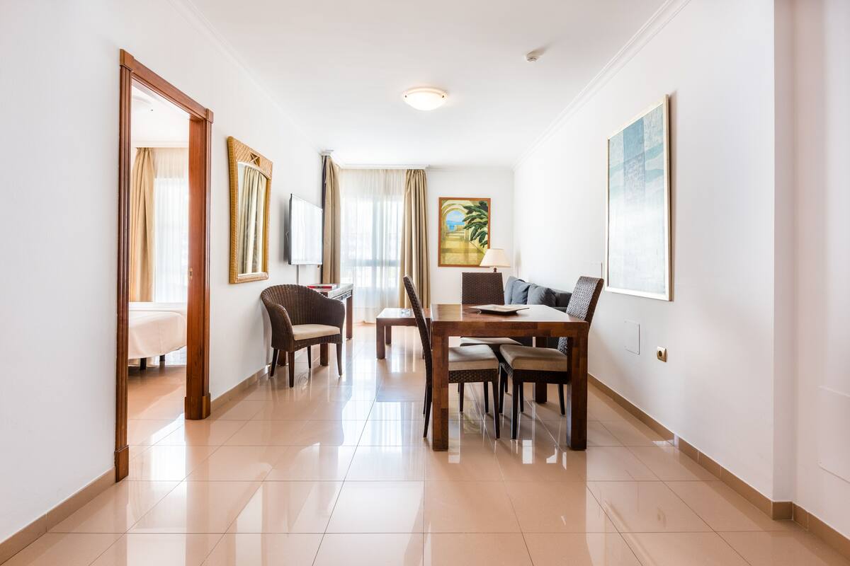 A hotel room with a dining area, a bed, a TV, and a window with curtains.