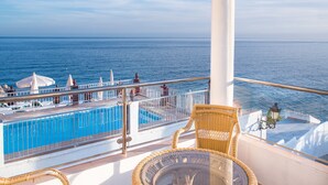 Un balcón con piscina, sillas de mimbre y vista al mar.
