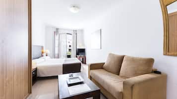 A hotel room with a bed, a sofa, a TV, and a window with curtains.