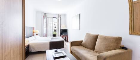 Een hotelkamer met een bed, een slaapbank, een televisie en een raam met gordijnen.