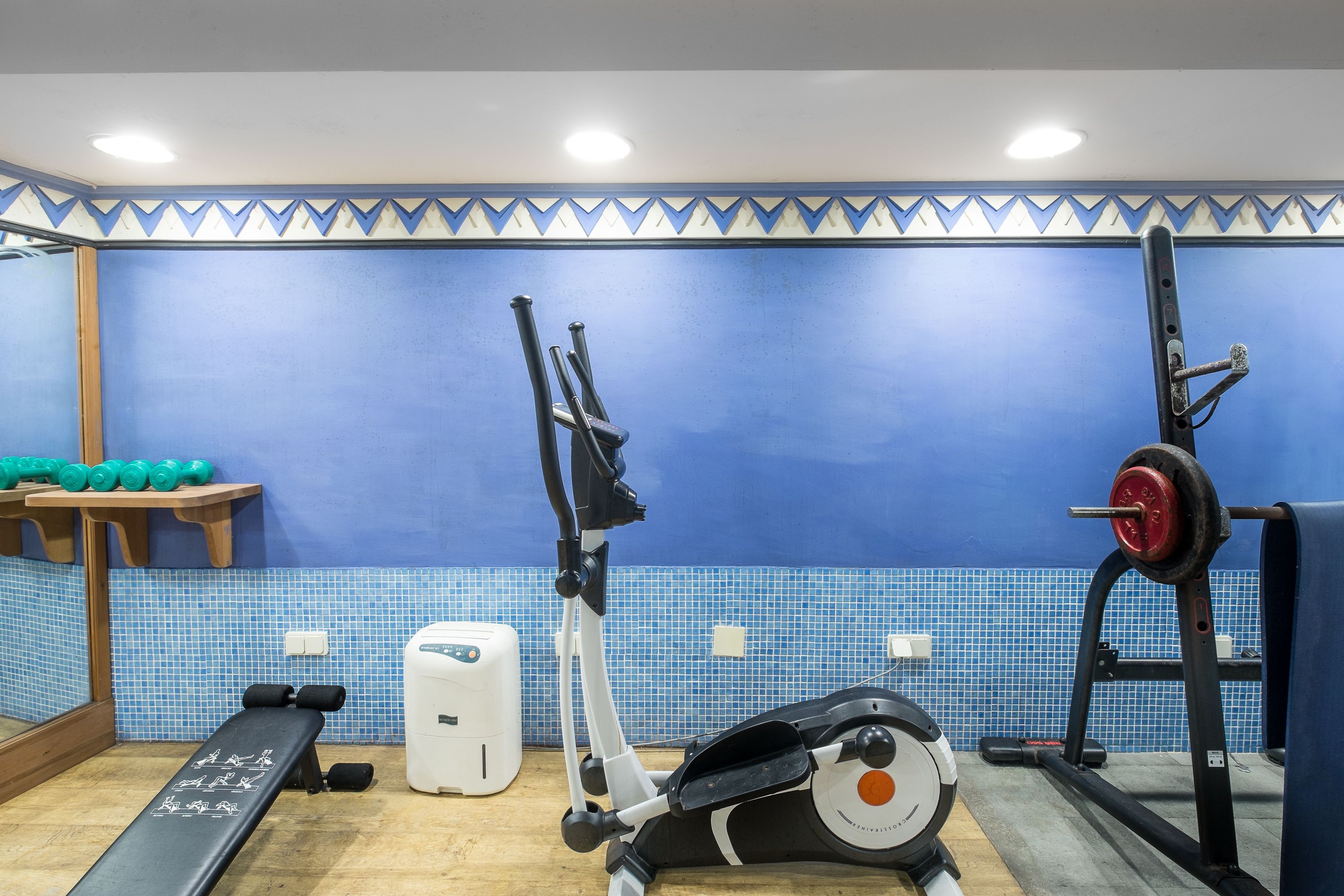 Un gimnasio con equipamiento de ejercicio, una banca y una pared de azulejos azules.