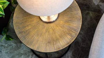 Primer plano de una lámpara con base metálica y pantalla circular texturizada.