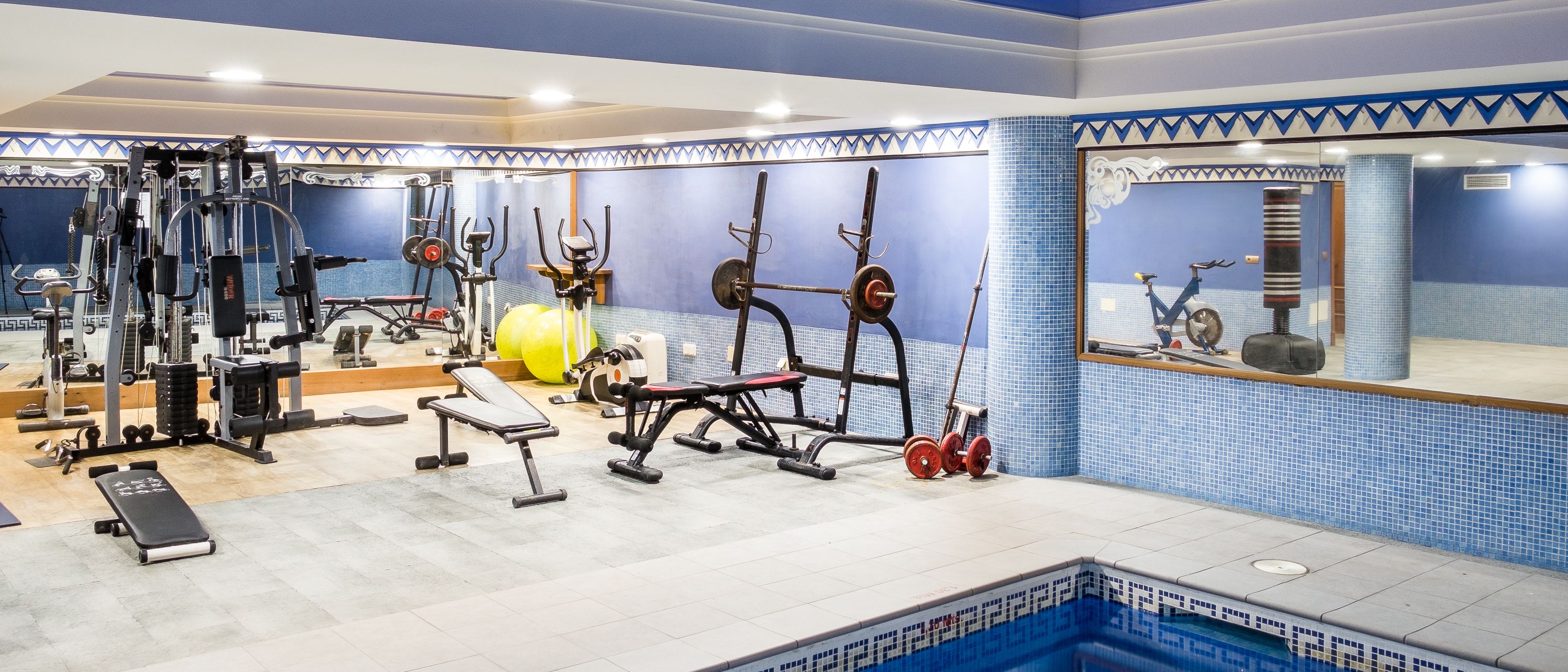 Un gimnasio con equipo de ejercicio diverso, una banca y una pequeña zona de piscina.