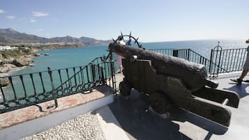 A cannon on a platform overlooking a coastal area with a clear view of the sea and distant mountains.