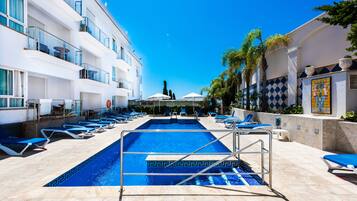 A pool area with lounge chairs, a diving board, and a clear blue sky.