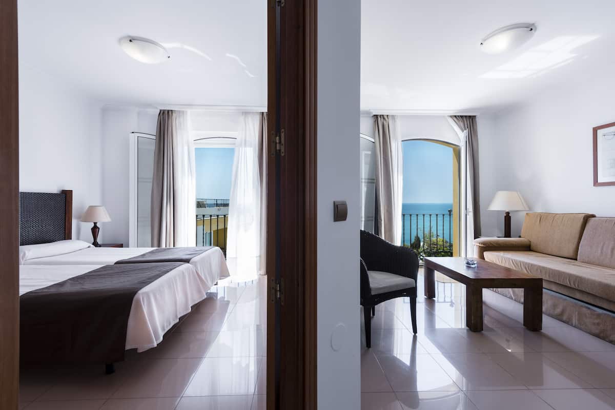 A hotel room with two beds, a sofa, a coffee table, and a balcony with a view.