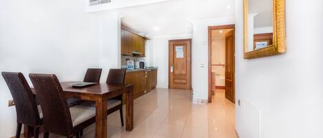 Un comedor con una mesa y sillas de madera, una cocina al fondo y un espejo en la pared.