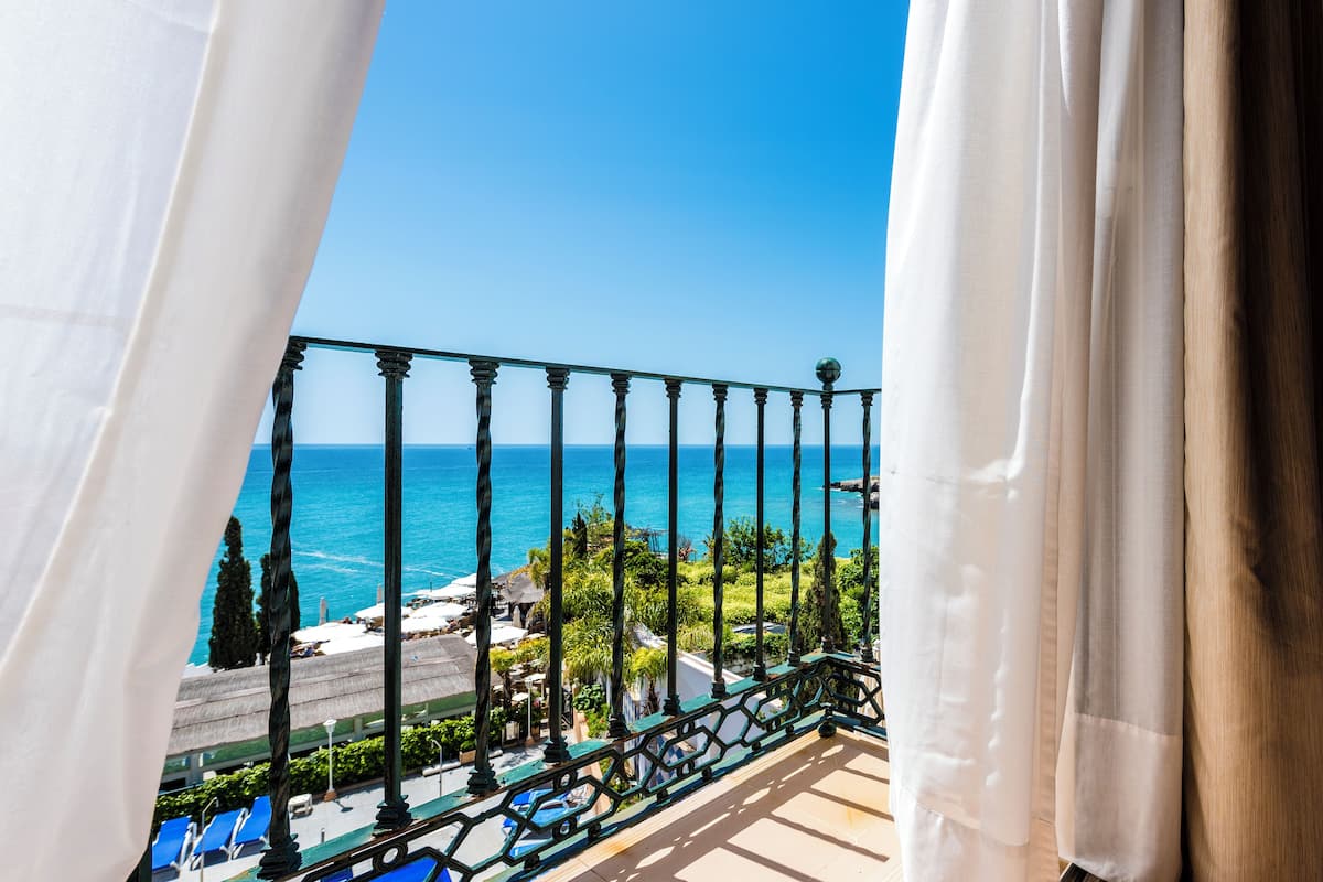 A balcony with a view of the sea, a railing, and some greenery.