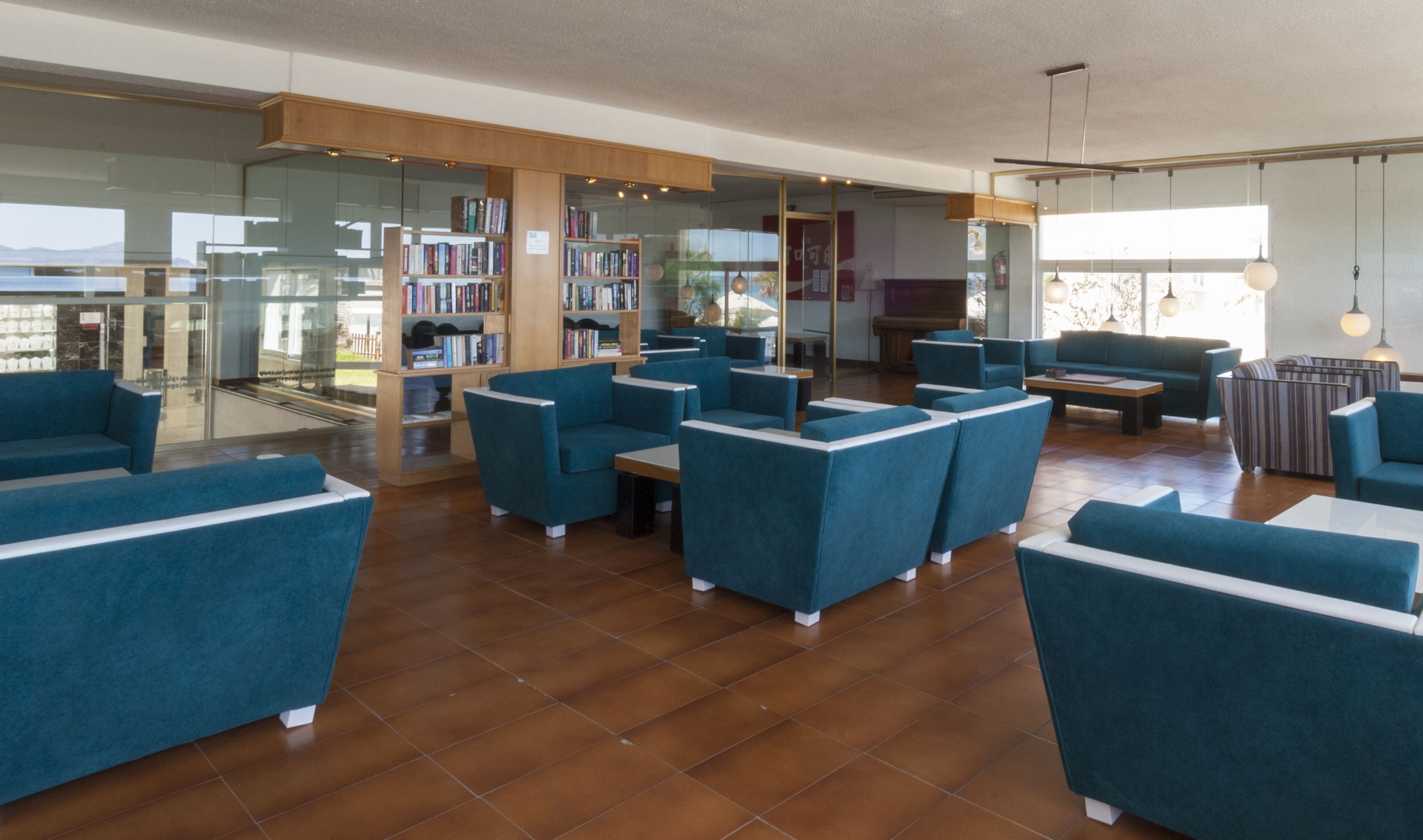 Un área de estar moderna con sofás azules, una estantería de madera y un separador de vidrio.