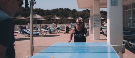 A beachside table tennis setup with a net, a table, and a paddle.