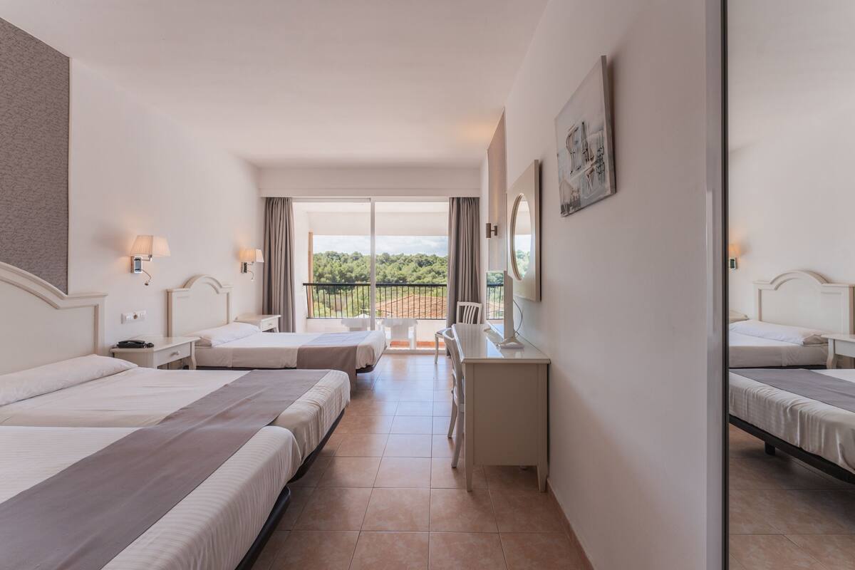 Hotelkamer met twee bedden, een bureau en een balkon met uitzicht op groen.