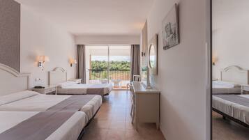 Habitación de hotel con dos camas, un escritorio y un balcón con vistas a zonas verdes.