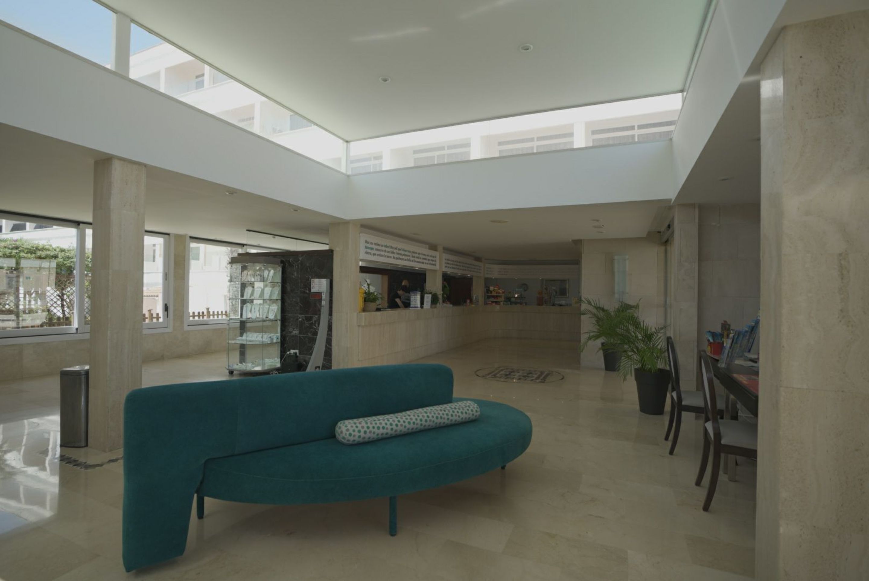 Un amplio vestíbulo con un sofá color turquesa, un mostrador de recepción y una planta en maceta.