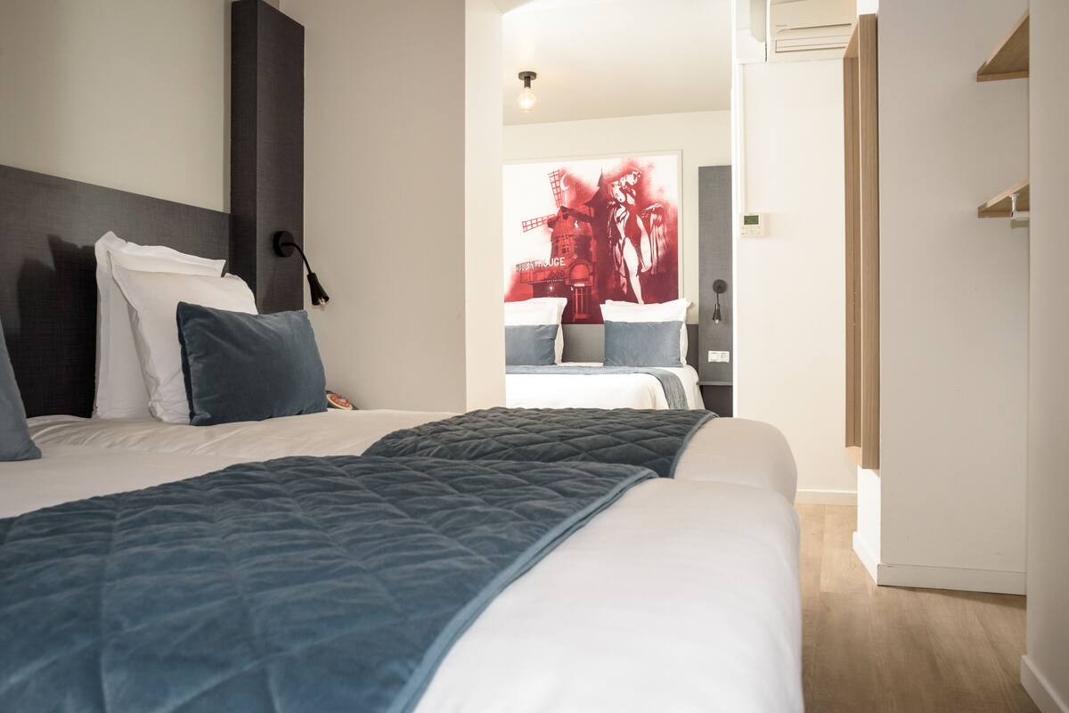 Une chambre d’hôtel moderne avec un grand lit, une table de chevet, une petite table et une lampe fixée au mur.