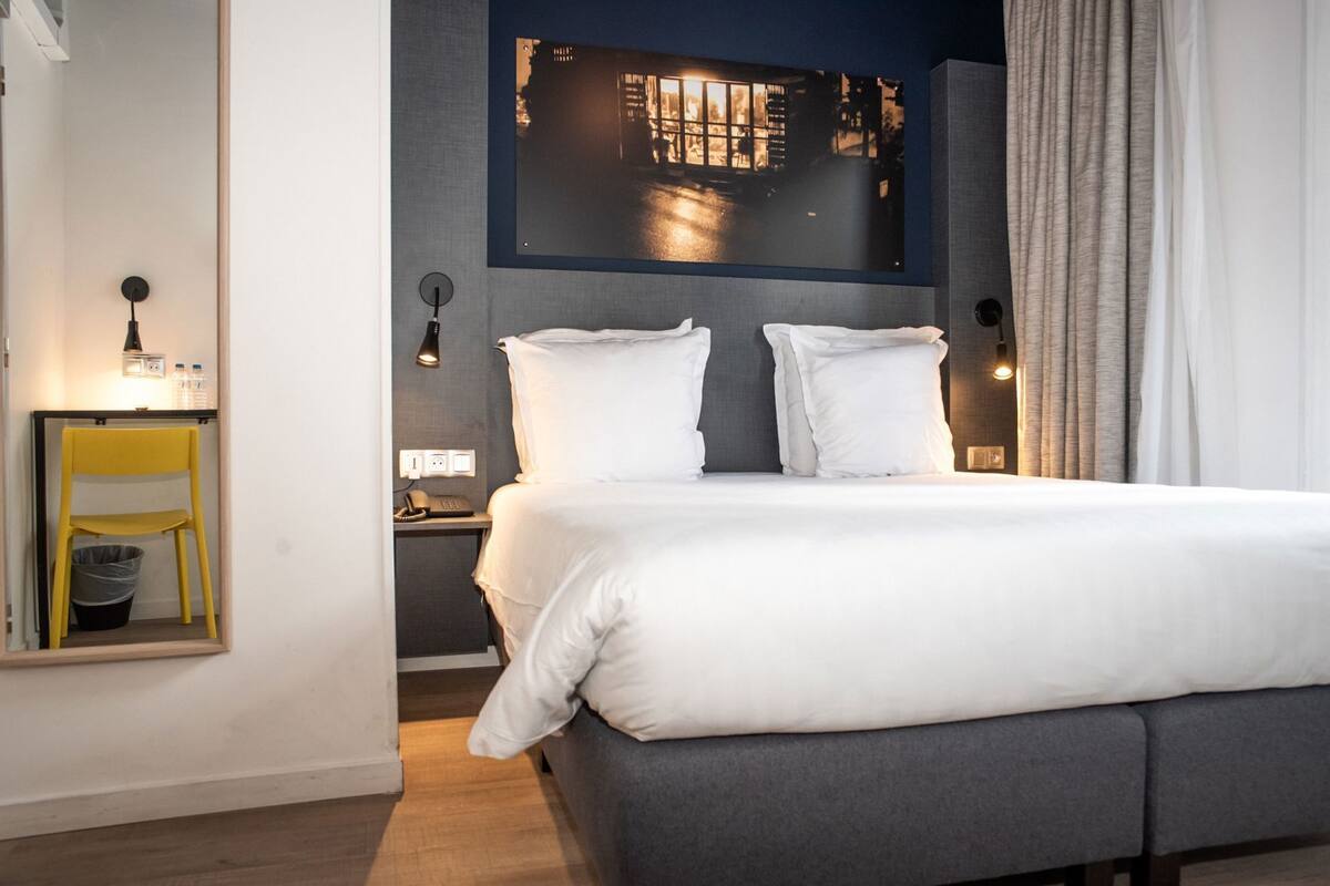 Une chambre d’hôtel moderne avec un grand lit, une table de chevet, une chaise et un miroir.