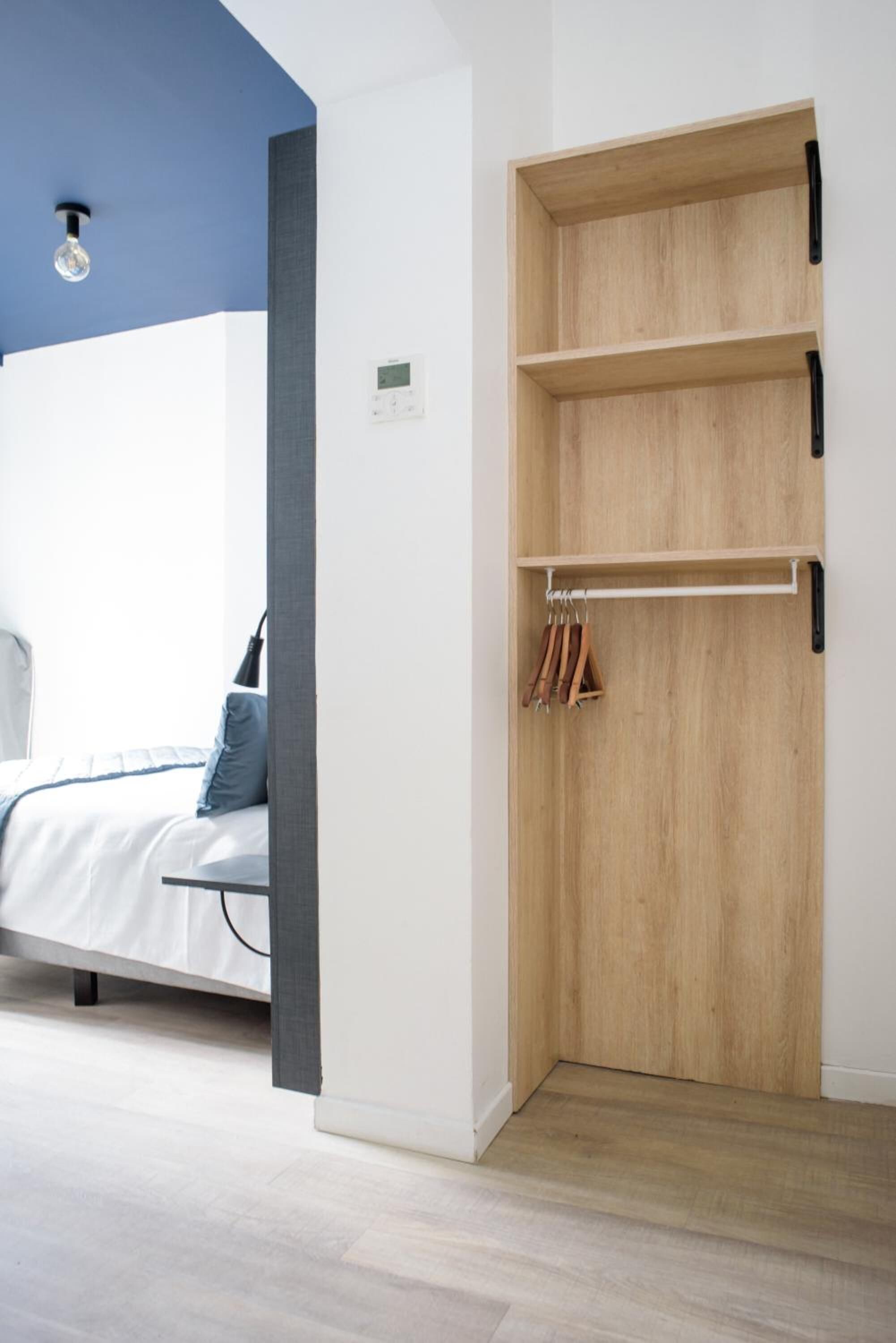 A bedroom with a bed, a wooden wardrobe, and a light fixture on the ceiling.