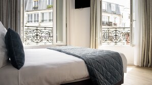 Un dormitorio con cama, cortinas y vistas a edificios a través de una ventana.