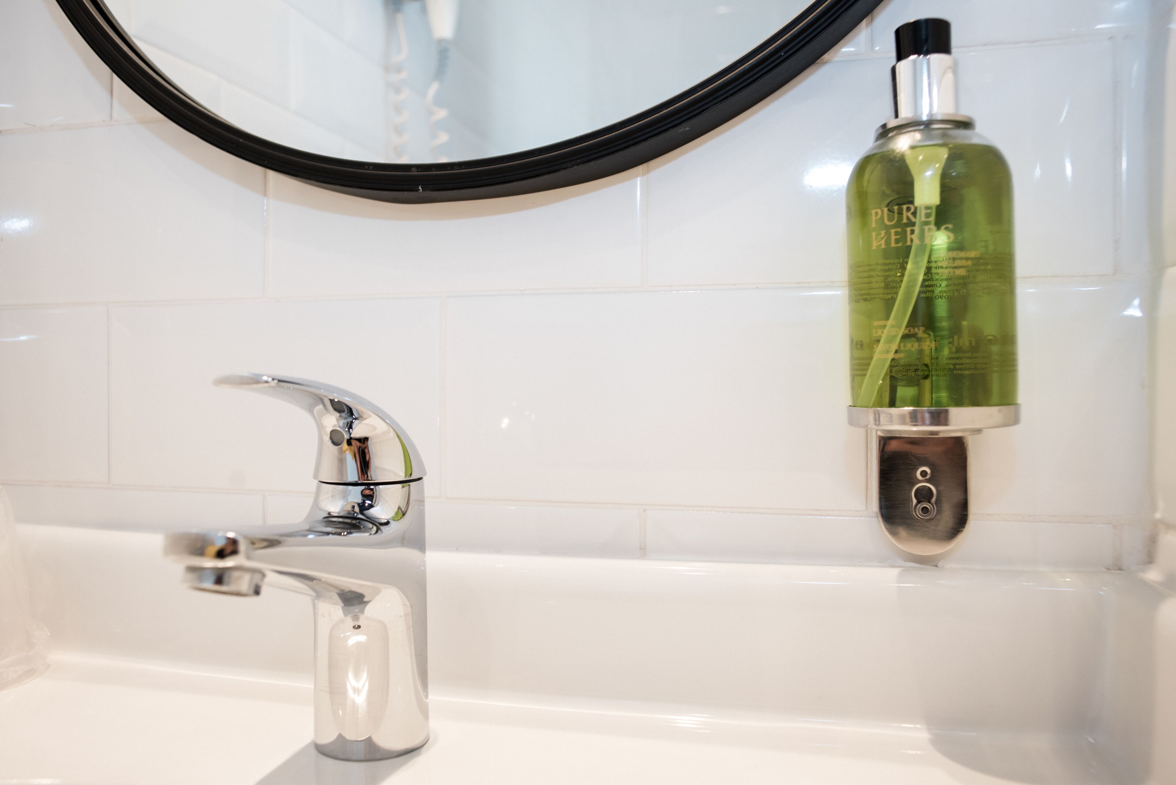 A bathroom with a chrome faucet and a green bottle of Pure Kerese soap on the wall.