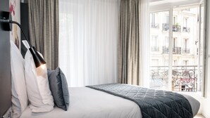 Una habitación de hotel con una cama, una lámpara de noche y vistas a un balcón con edificios.