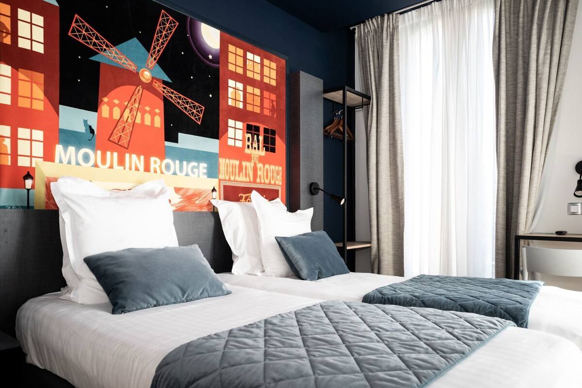 Une chambre d’hôtel avec deux lits, une table de chevet, une lampe et une vue sur la Tour Eiffel.