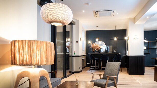 Un interior moderno con una mesa de centro de madera, una silla, una lámpara y una cocina al fondo.