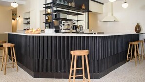 Una cocina moderna con una isla central, taburetes de bar, iluminación colgante y un salpicadero negro.