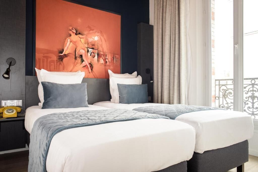 A double bed with a grey and white duvet, two pillows, a bedside table with a yellow telephone, and a large abstract painting on the wall.