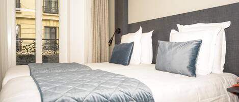 A hotel room with a bed, a headboard, a window with curtains, and a view of a building outside.