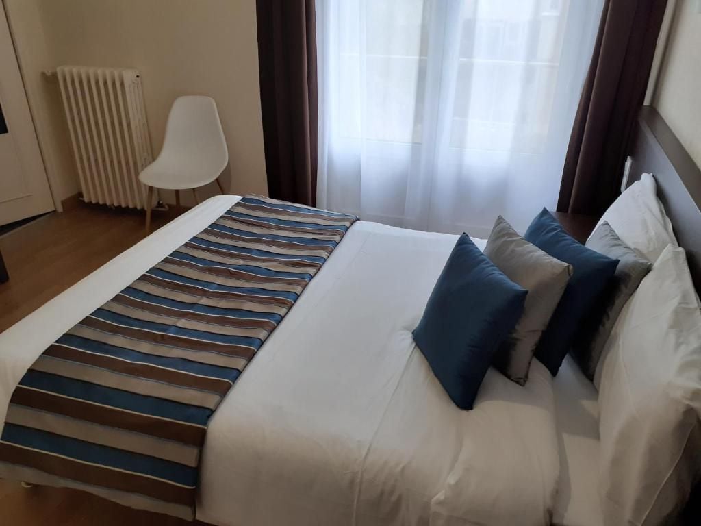 A hotel room with a bed, a chair, a radiator, and a window with curtains.