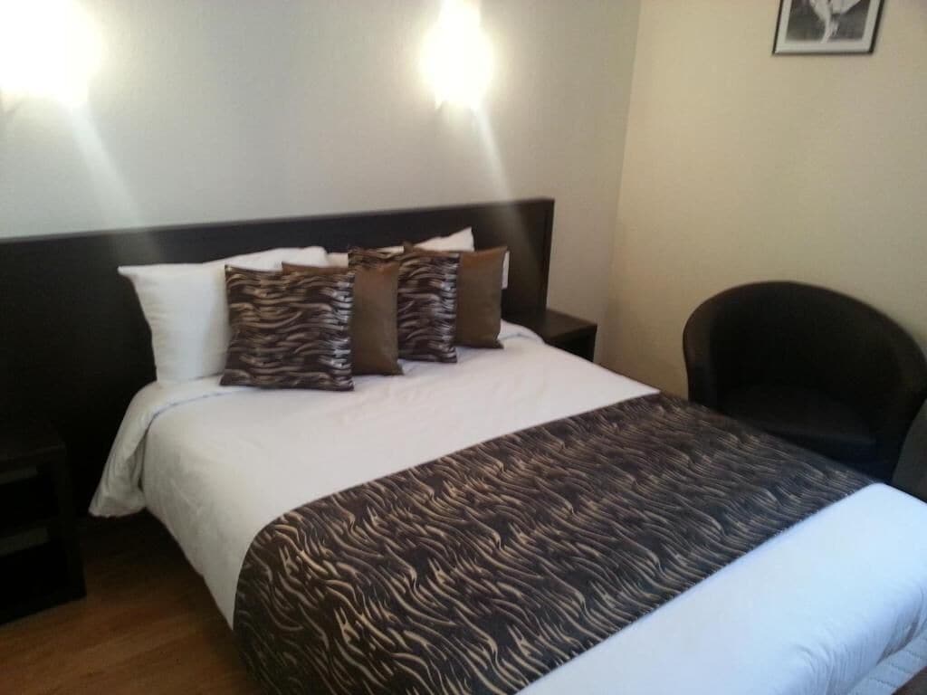 Ein Hotelzimmer mit einem Bett, zwei Nachttischen, einem Sessel und einer Wandleuchte.