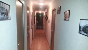 Un pasillo con suelo de madera y puertas a ambos lados, que conduce a una habitación con un letrero de salida verde.