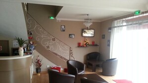 Un vestíbulo de hotel con recepción, escalera, zona de estar y televisor.