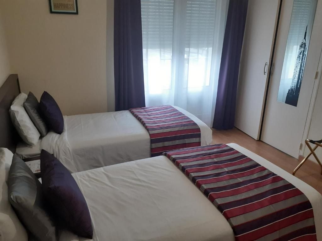 Una habitación de hotel con dos camas, una ventana con cortinas y un cuadro en la pared.