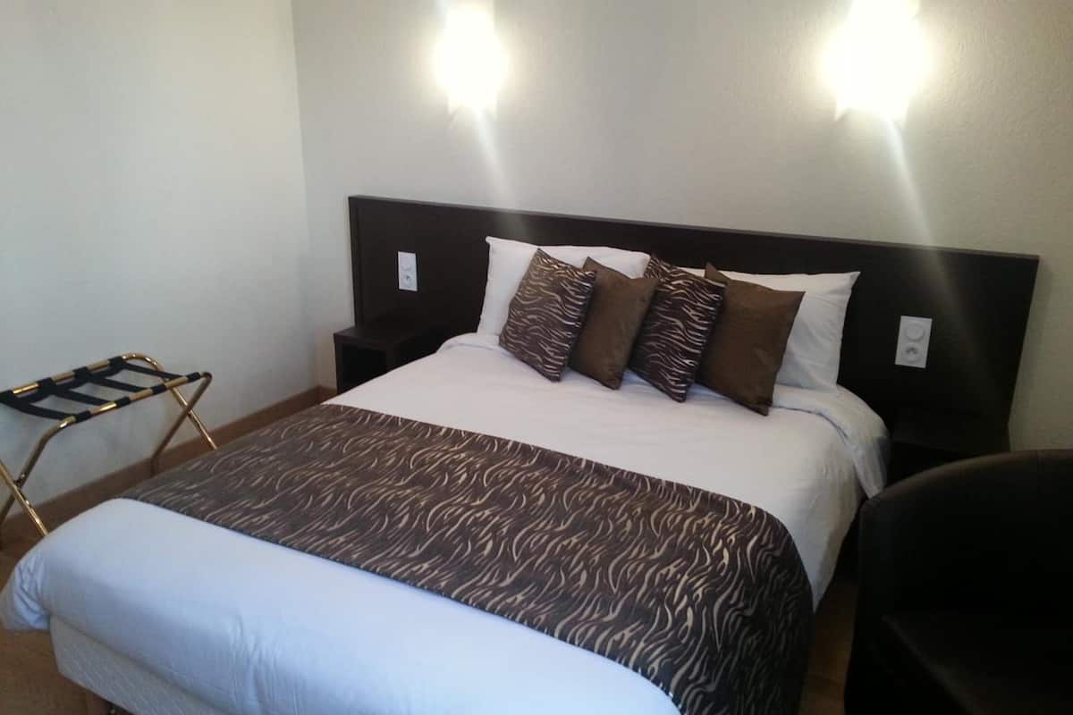 A hotel room with a bed, a nightstand, a chair, and two wall-mounted lights.
