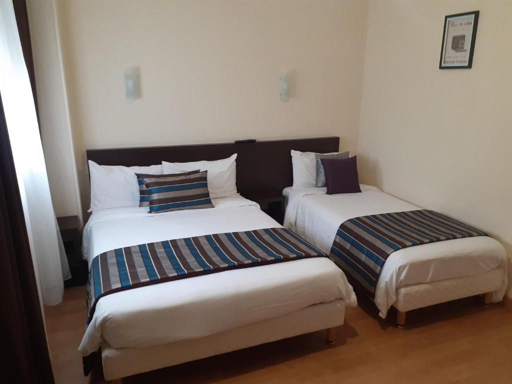 Een hotelkamer met twee bedden, elk met een streepjesbeddeken en kussens.