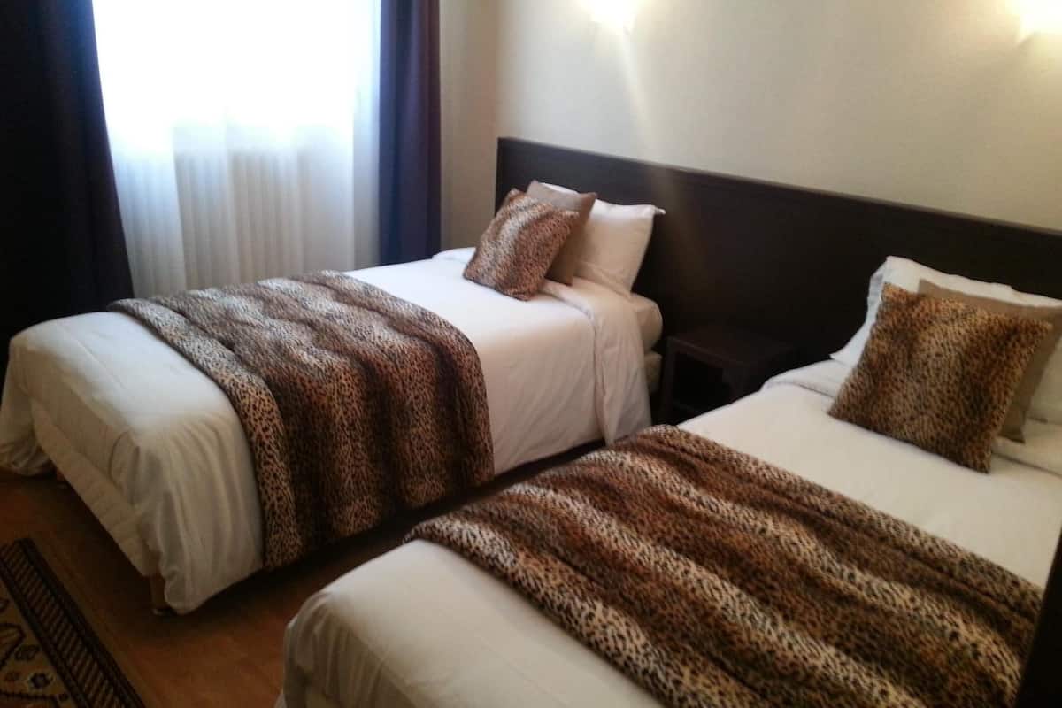 Two single beds with matching headboards and pillows, a window with curtains, and a wall-mounted light fixture.