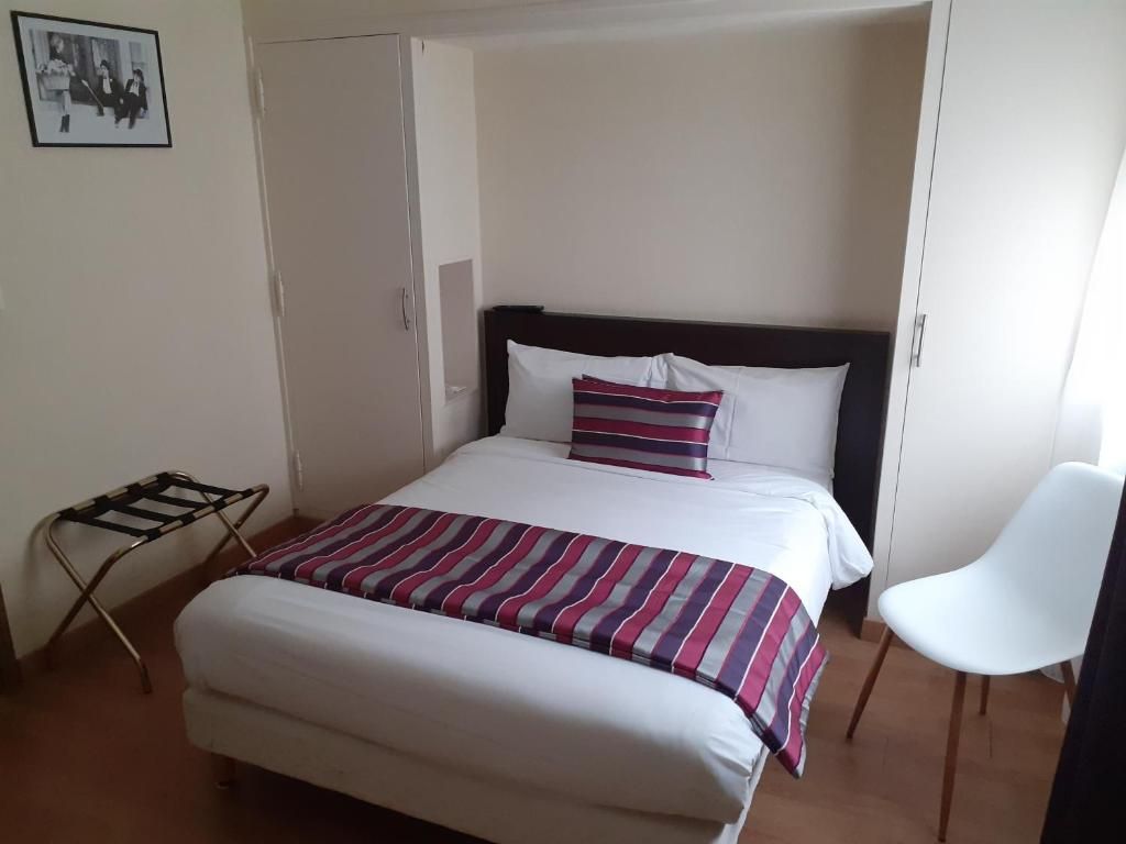 Un lit simple avec une couverture à rayures, une chaise blanche et une armoire dans une pièce aux murs unis.