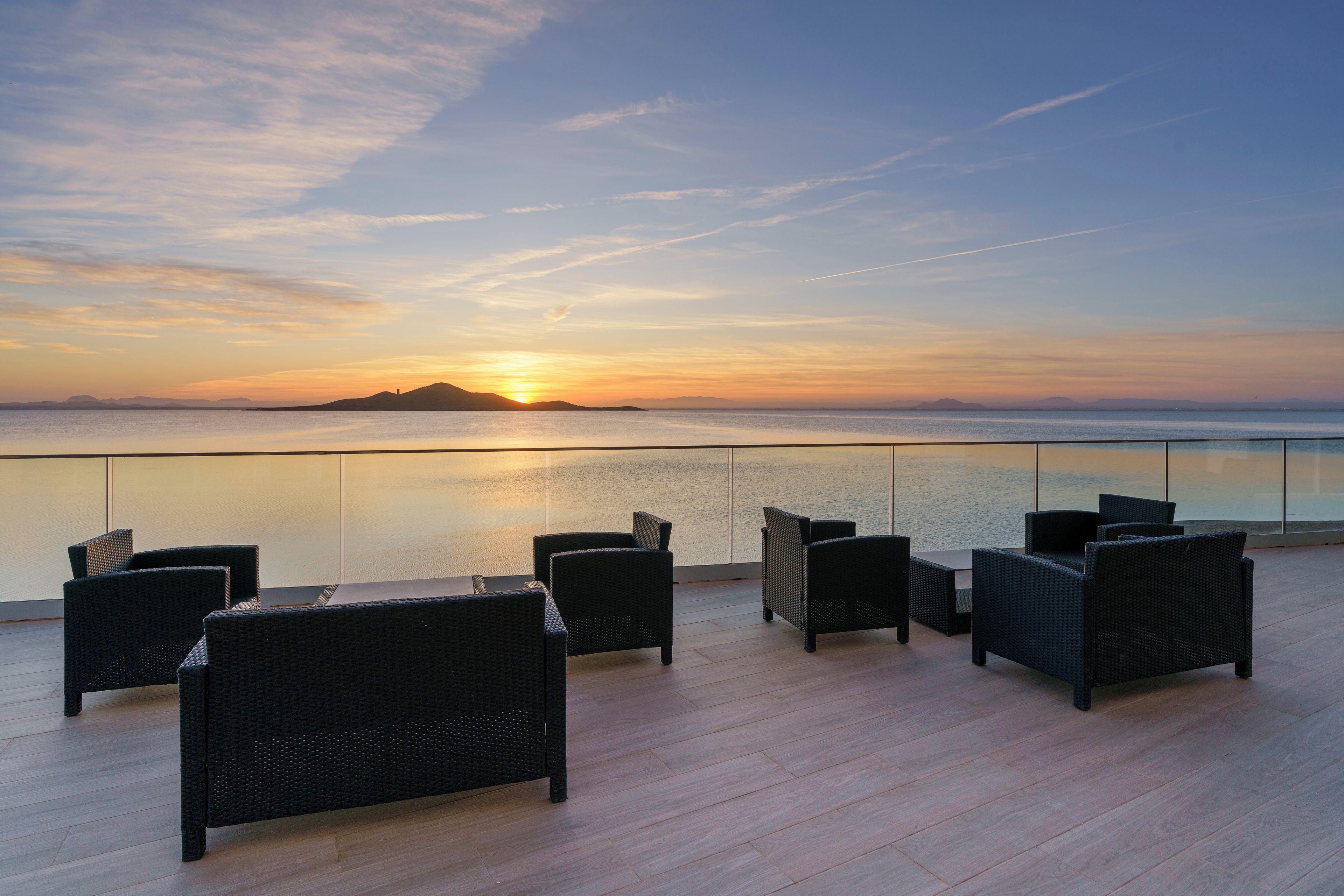 Una terraza con muebles de mimbre que da a un mar tranquilo al atardecer.