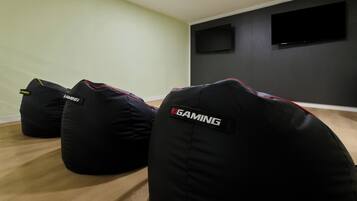 Sillones de felpa con la etiqueta 'RGAMING' en una habitación con suelo de madera y un televisor de pantalla plana montado en la pared.