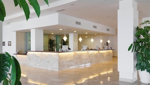 A modern reception area with a marble counter, pendant lighting, and potted plants. - Aluasun Doblemar (San Javier)