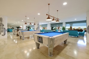 A pool table in a well-lit room with a ceiling fan and blue chairs.