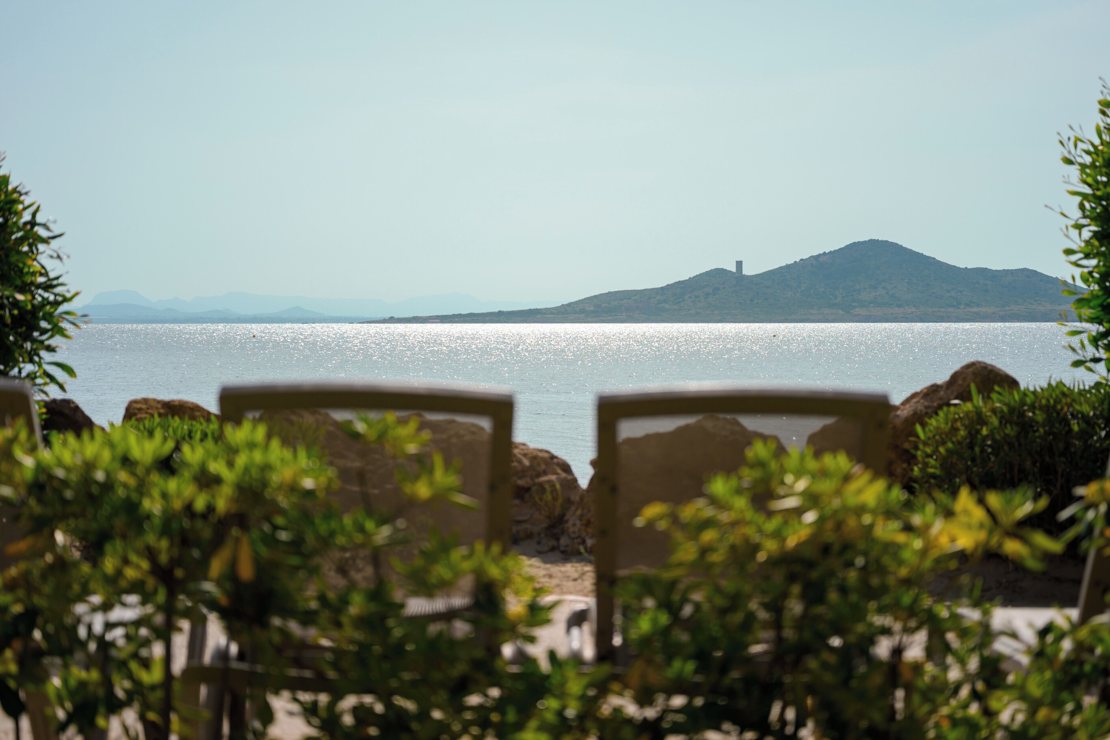 Une vue sur une plage avec des chaises disposées face à la mer, une montagne en arrière-plan et un ciel dégagé.