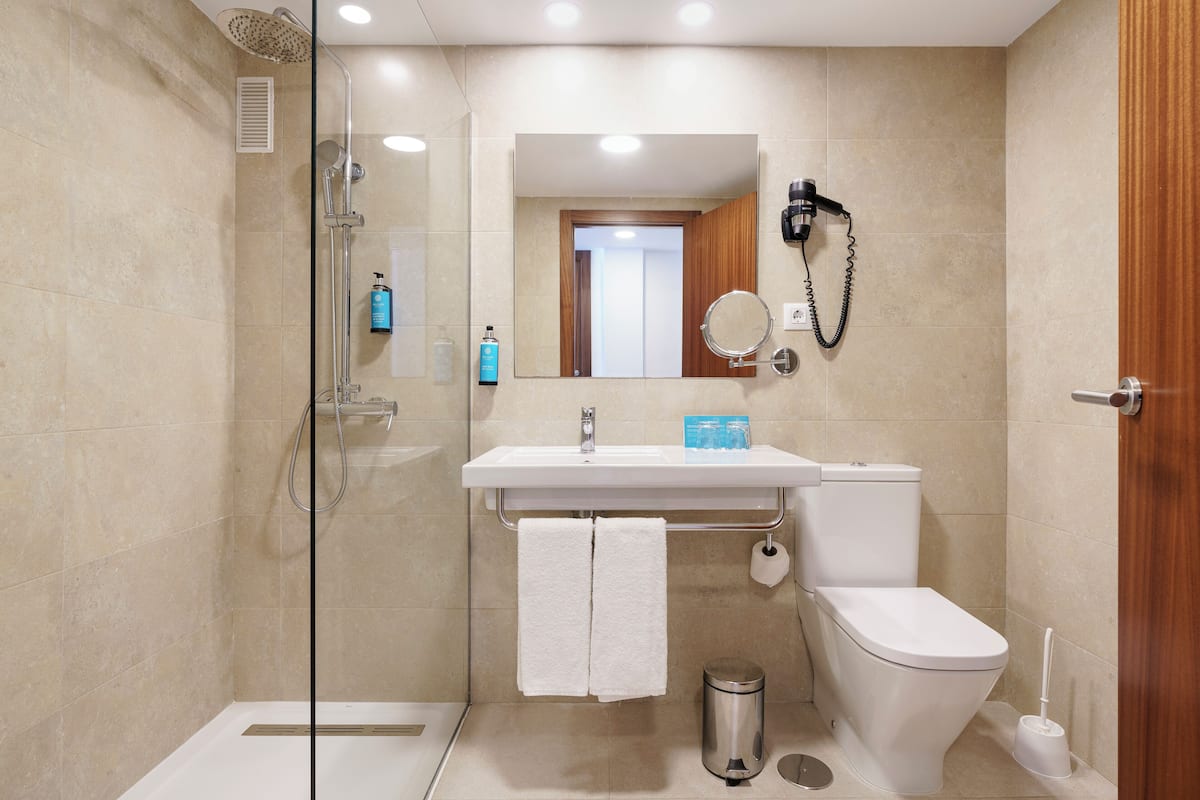 A modern bathroom with a glass-enclosed shower, a white sink with a mirror, and a toilet.