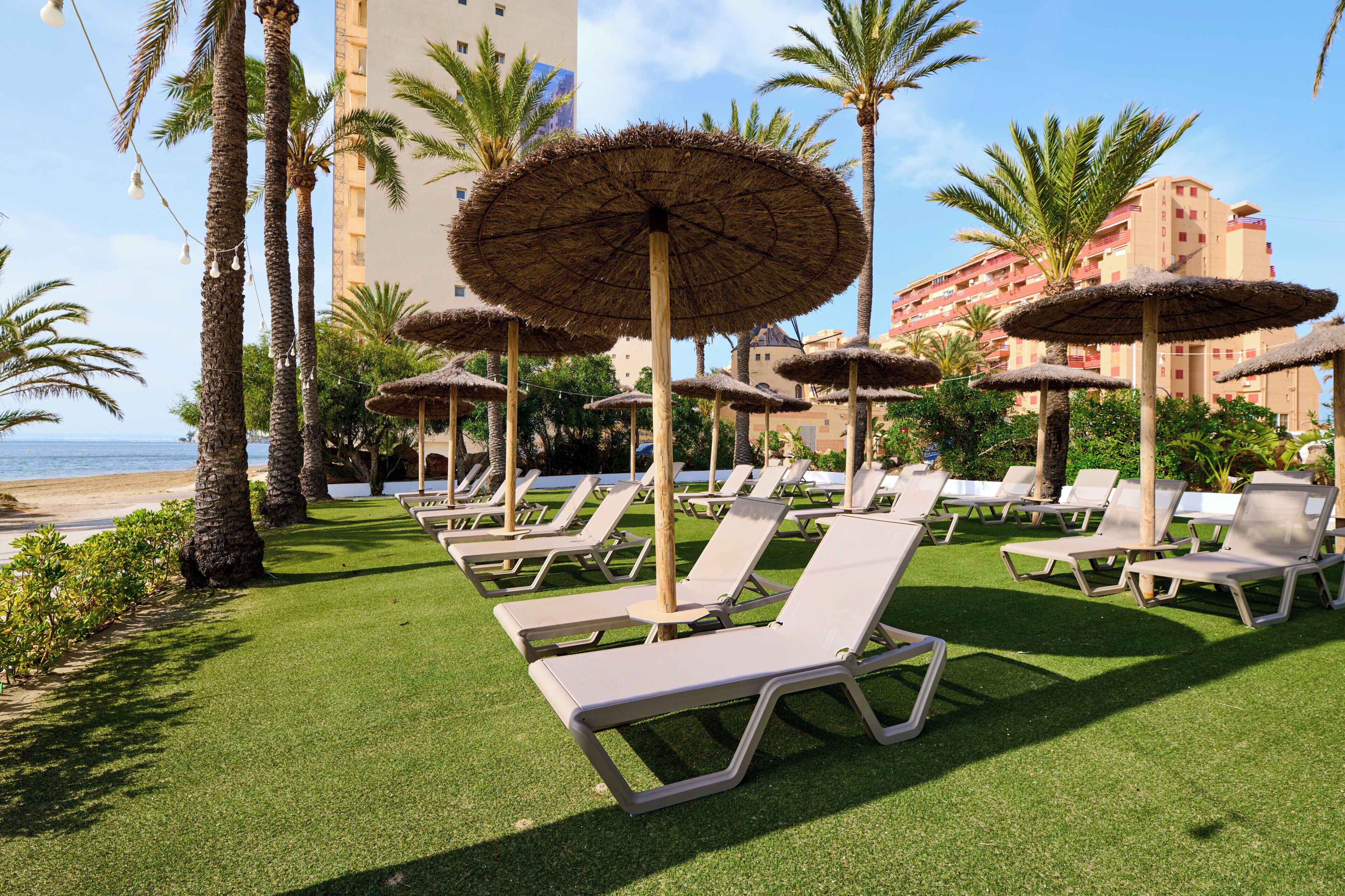 Un resort con tumbonas, sombrillas de paja y palmeras.