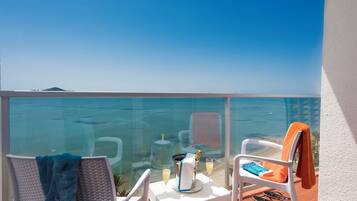 Un balcón con vista despejada al mar, dos sillas, una mesa con una botella y vasos, y una toalla colgada en una silla.