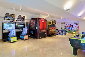 An indoor arcade with various gaming machines, including racing and claw machines, and a pool table.