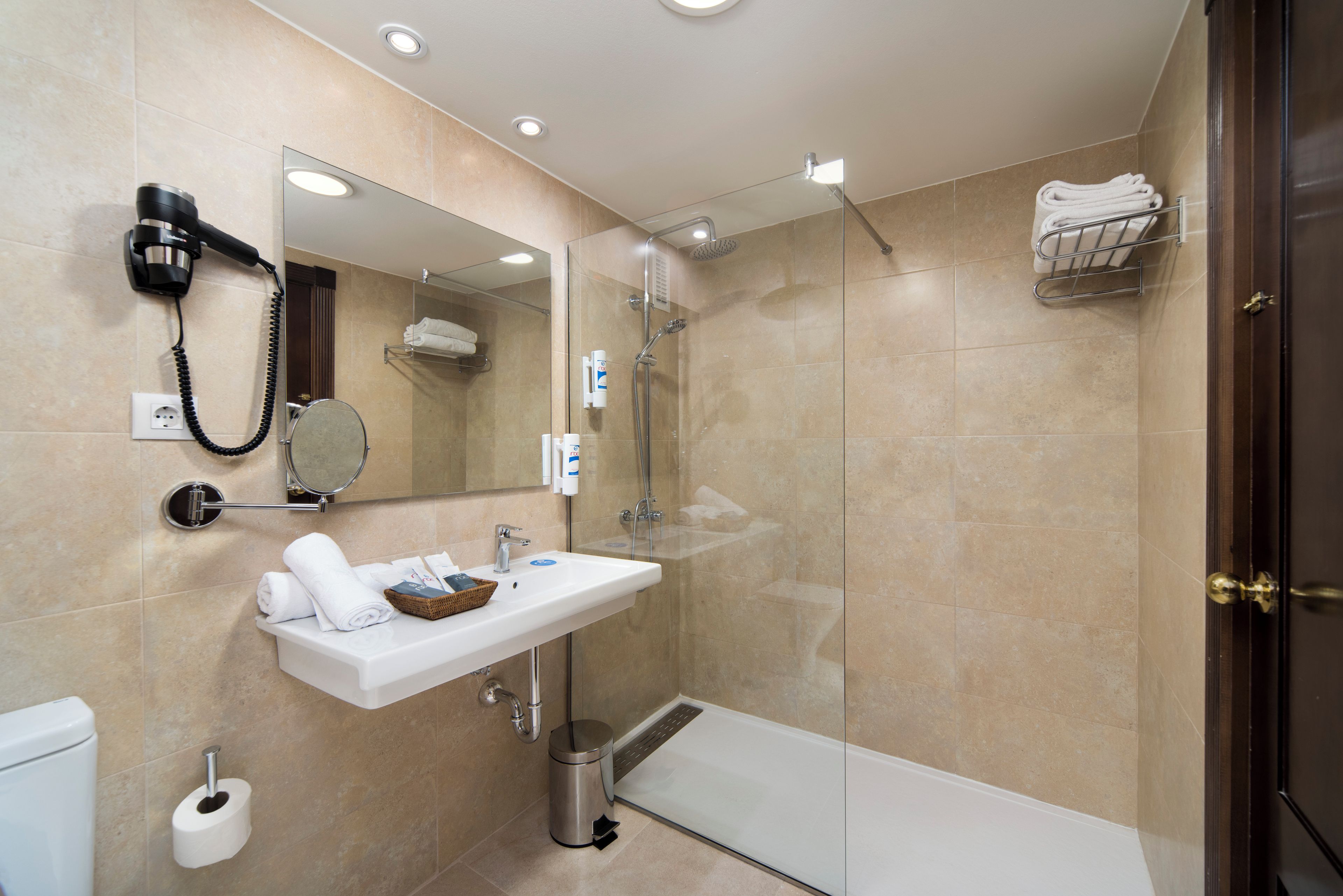 Une salle de bain moderne dotée d’une douche à parois de verre, d’un lavabo blanc avec un porte-serviettes et d’un sèche-cheveux fixé au mur.